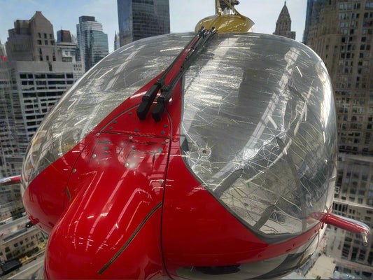 Red ambulance helicopter on roof top in city with silver sunshield in windscreen