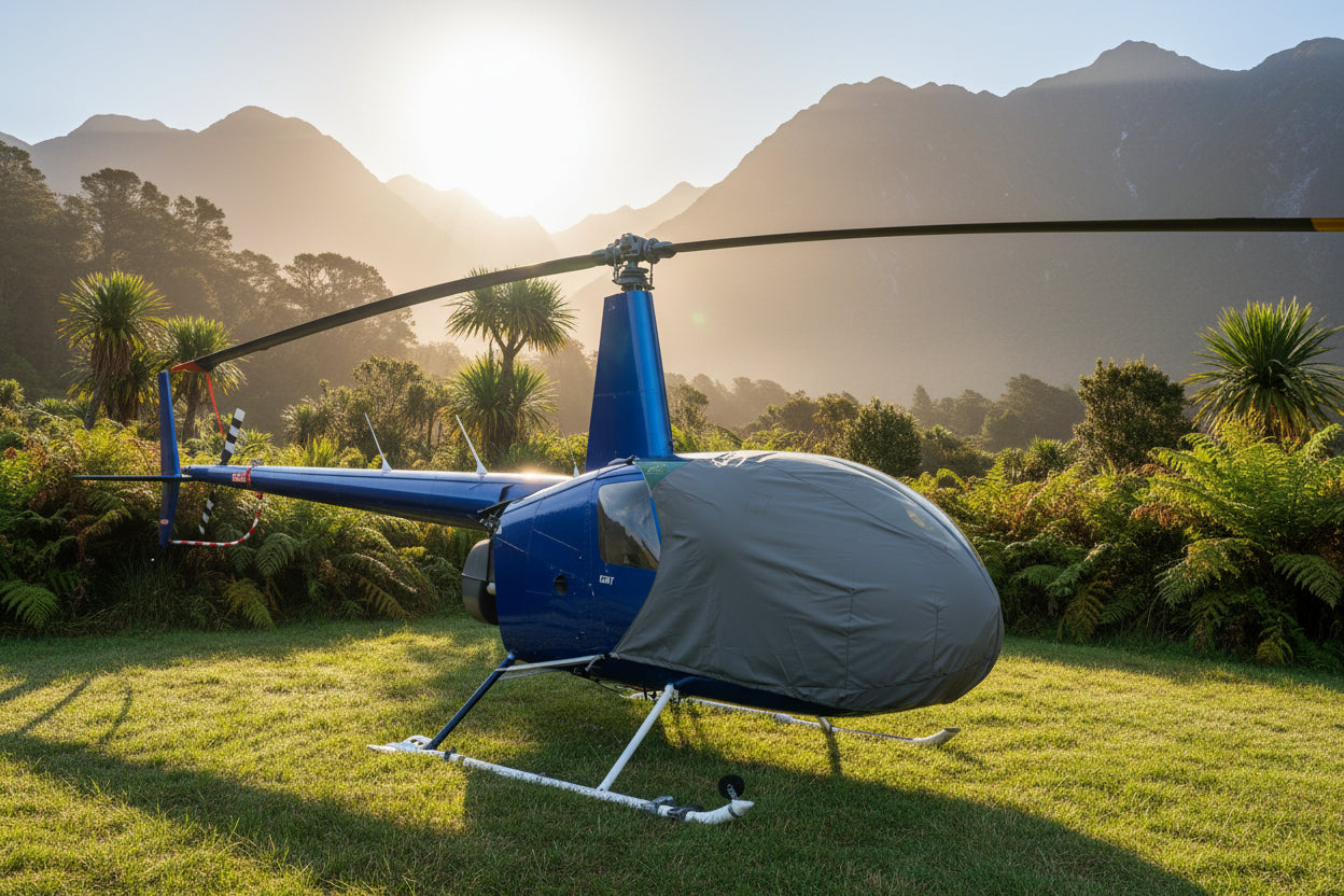 Blue helicopter with a grey aerosew  bubble cover on a grassy field under a rising sun