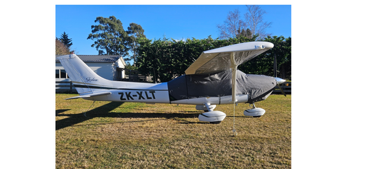 Cessna_182_side_on_grey_aerosew_canopy_cover_in_front_of_trees_and_house