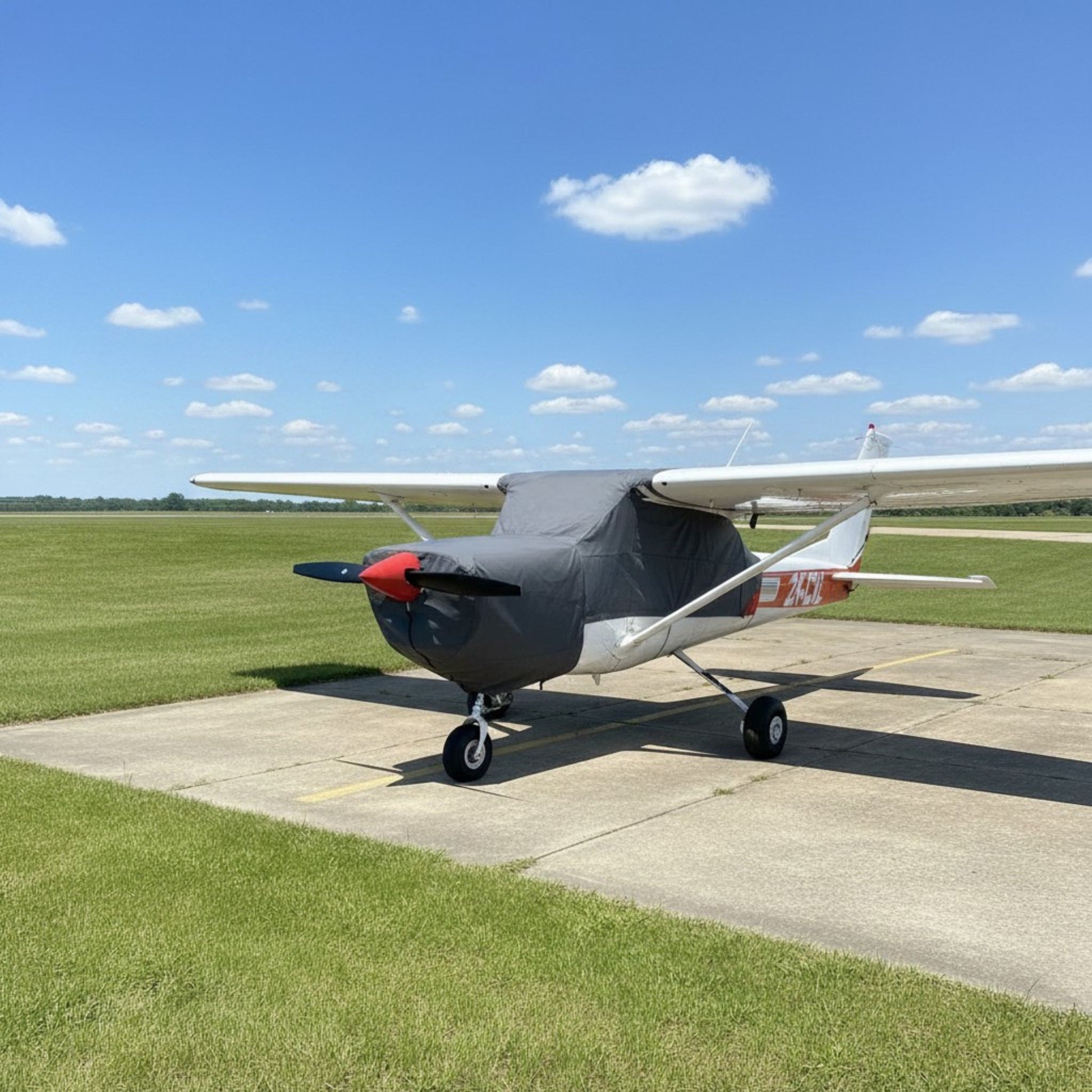 Red Cessna C152 with aerosew canopy cover with small aerodrome in background