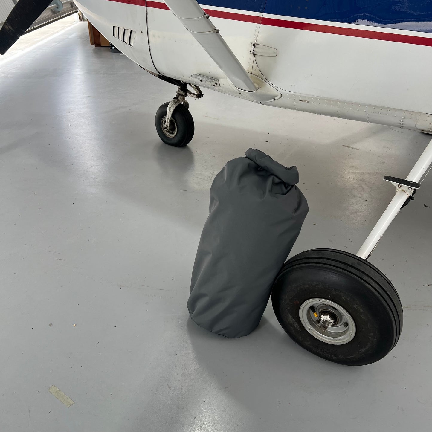 Small cessna C182 airplane wheel with a grey bag containing aerosew half cover beside wheel on a concrete surface