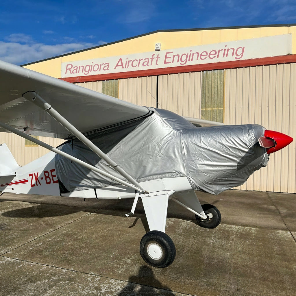 Small airplane with a aerosew cover parked in front of Rangiora Aircraft Engineering building.
