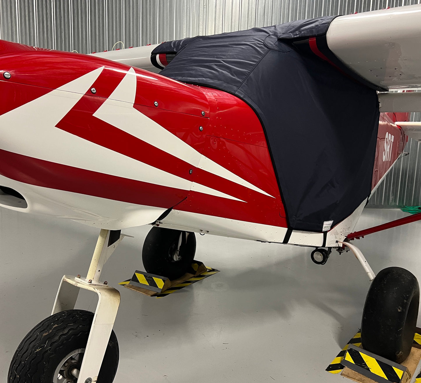 red aircraft in hangar with blue aerosew cover on. 