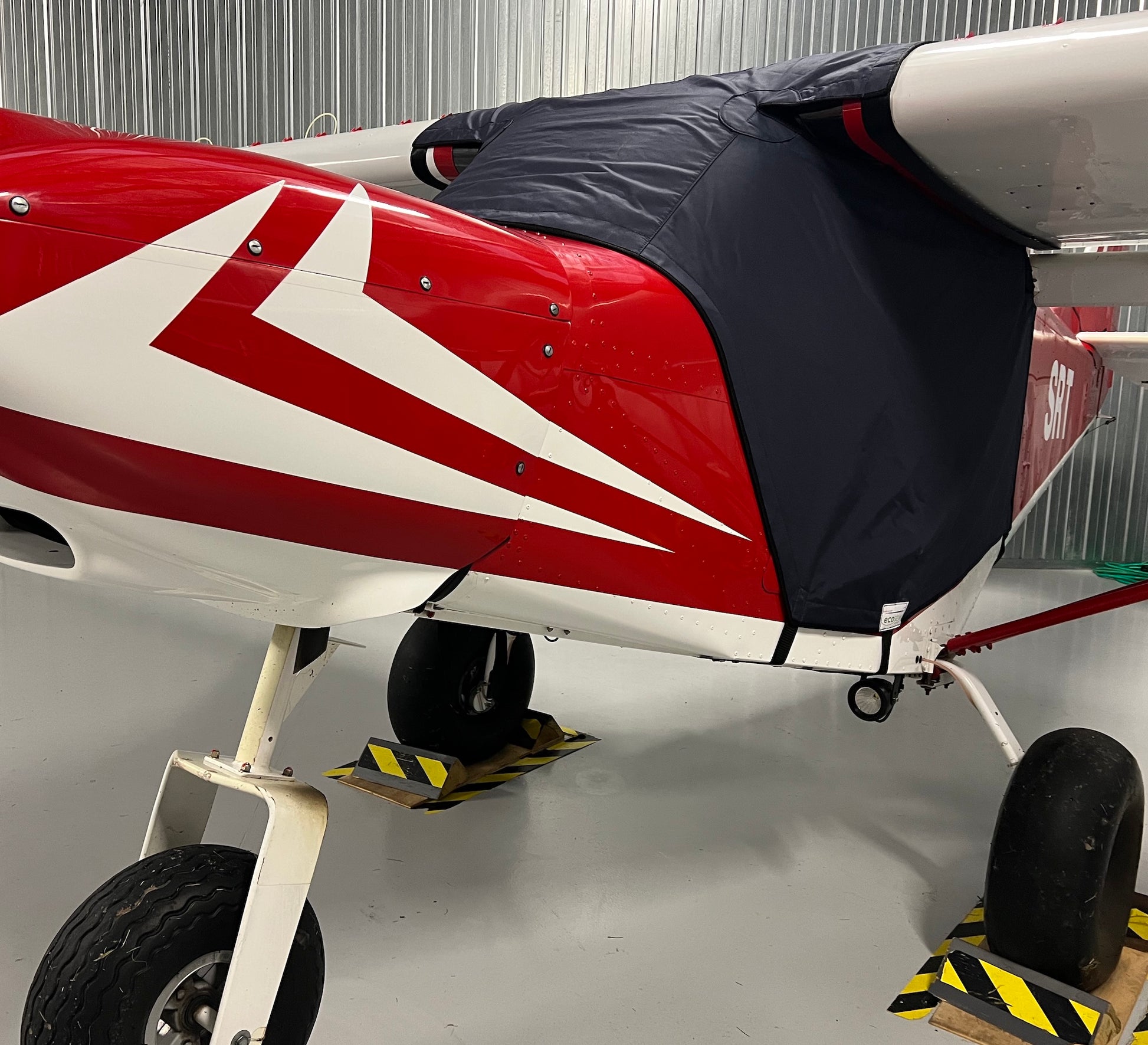 red aircraft in hangar with blue aerosew cover on. 