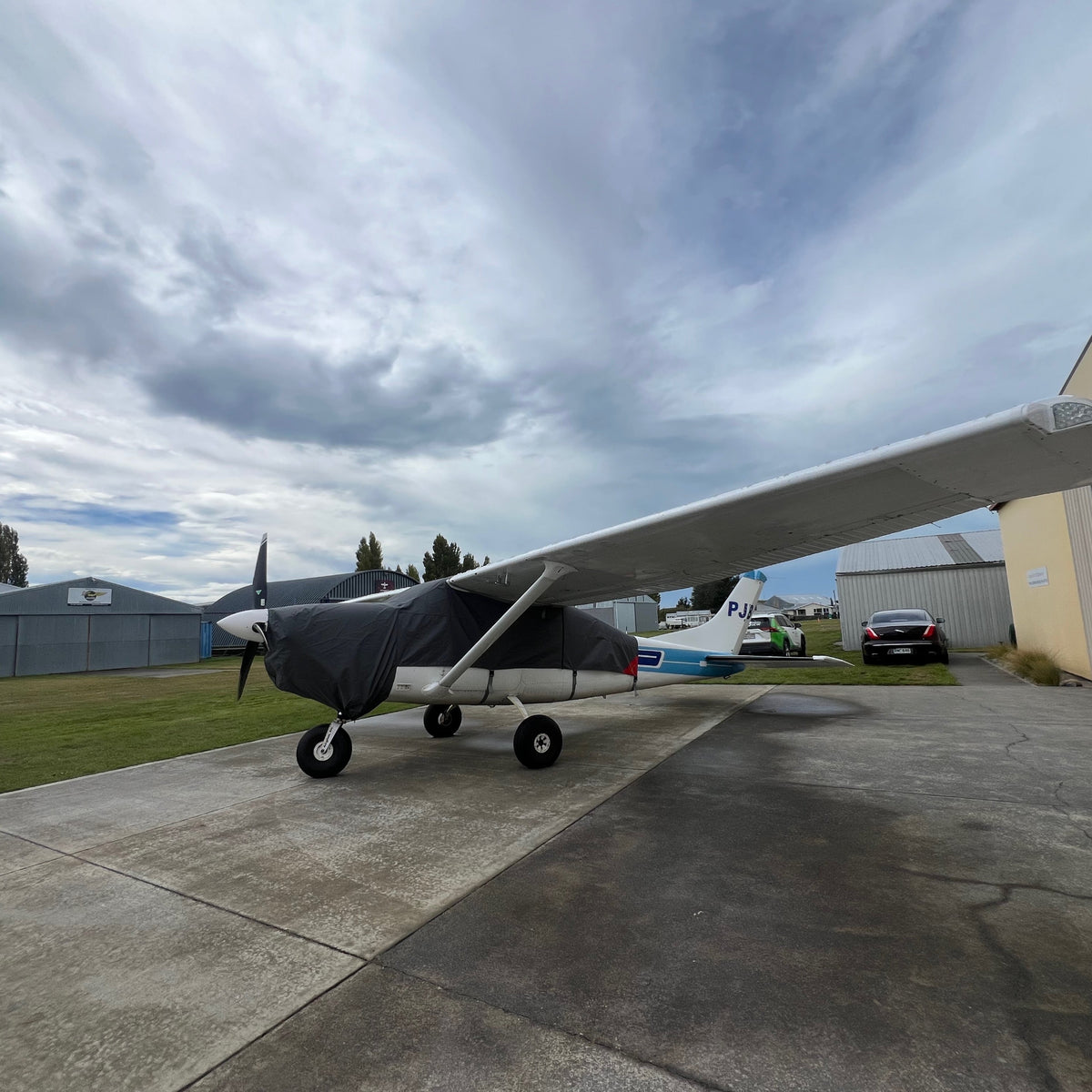 Front three-quarter view of a Cessna C206 fitted with a charcoal Aerosew canopy cover over the nose, cockpit and wing roots.