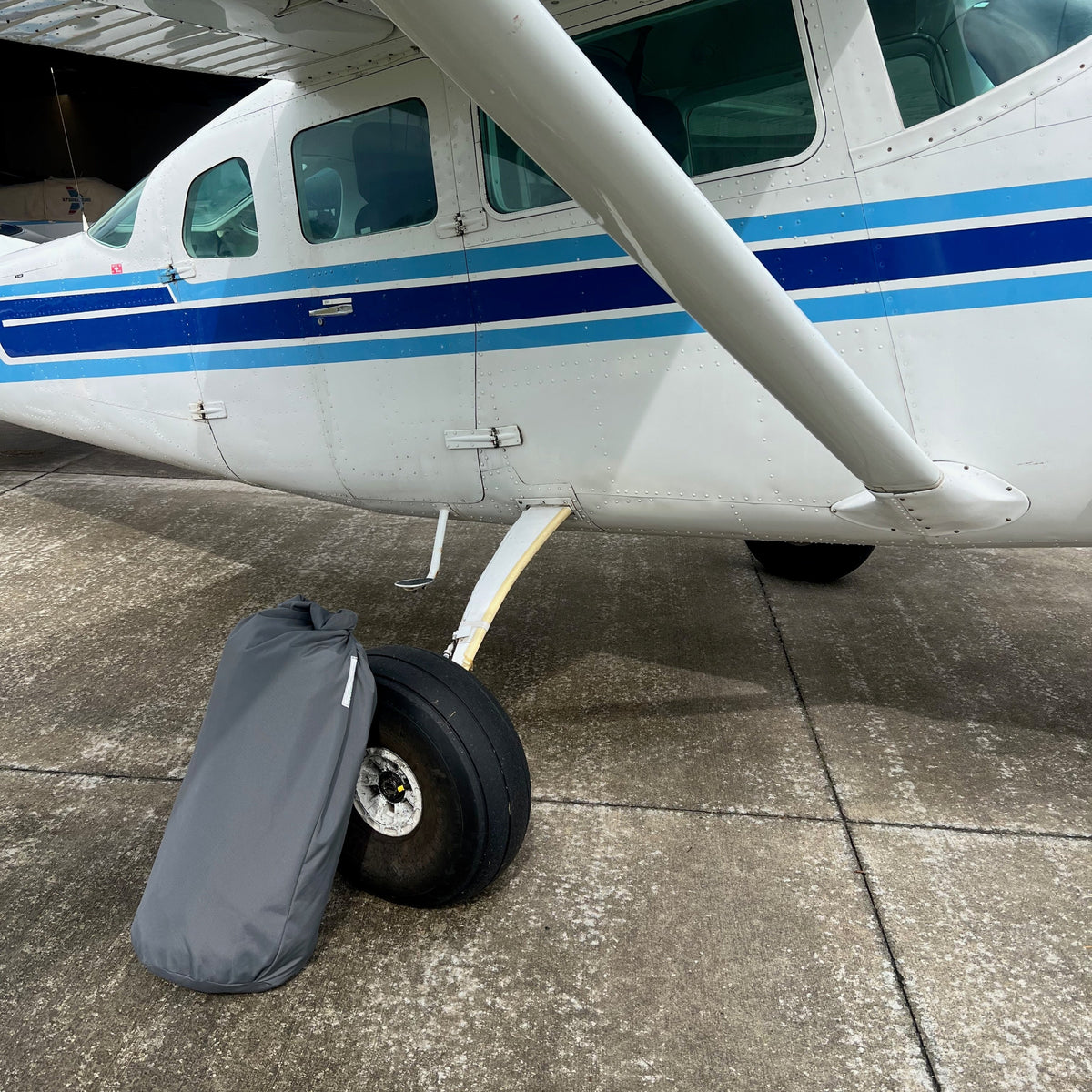 Charcoal Aerosew canopy-cover storage bag positioned beside the main wheel of an uncovered Cessna C206.