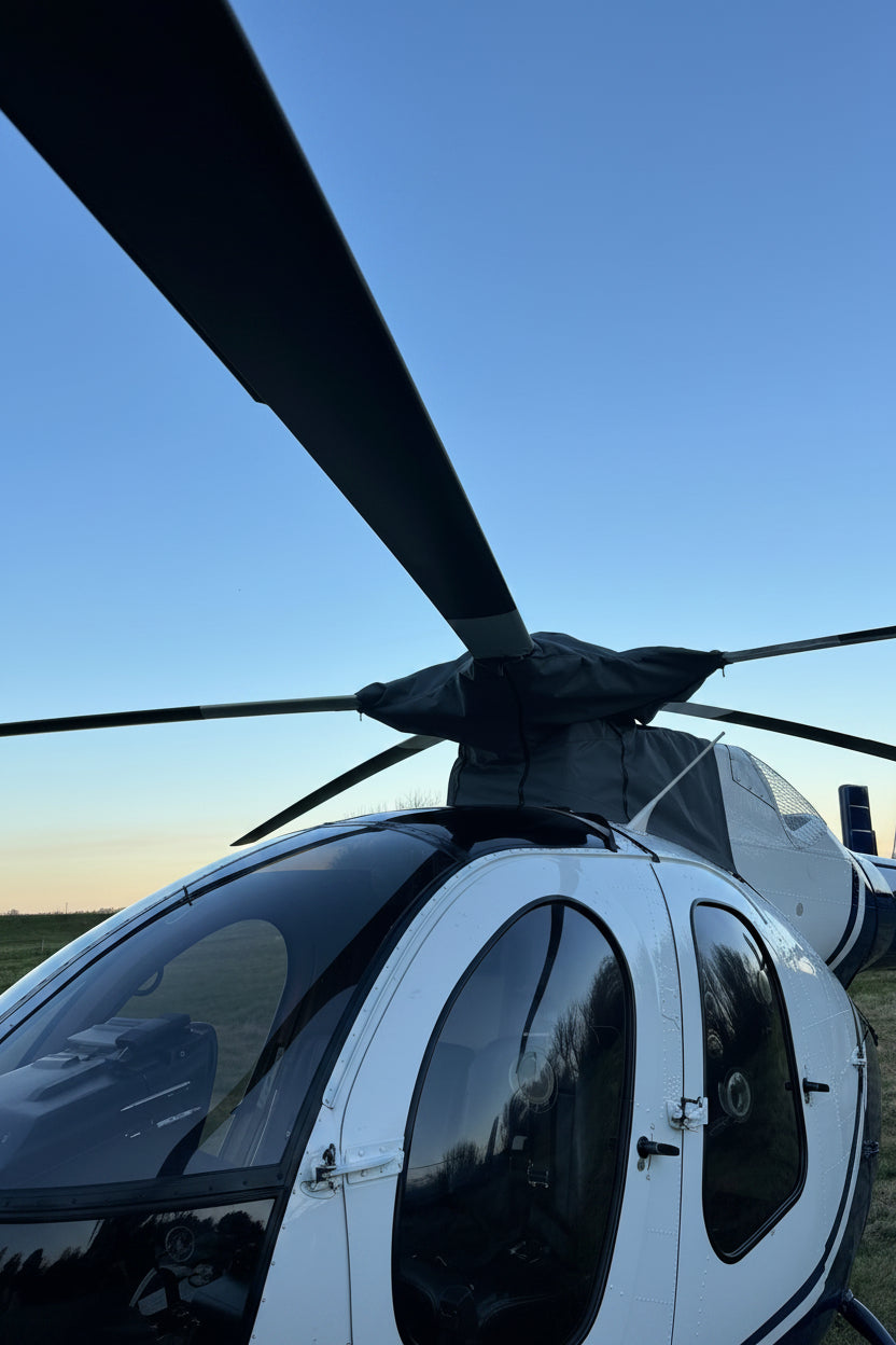 Front view of a white Hughes 500 helicopter fitted with a aerosew charcoal rotor head and transmission cover outdoors.