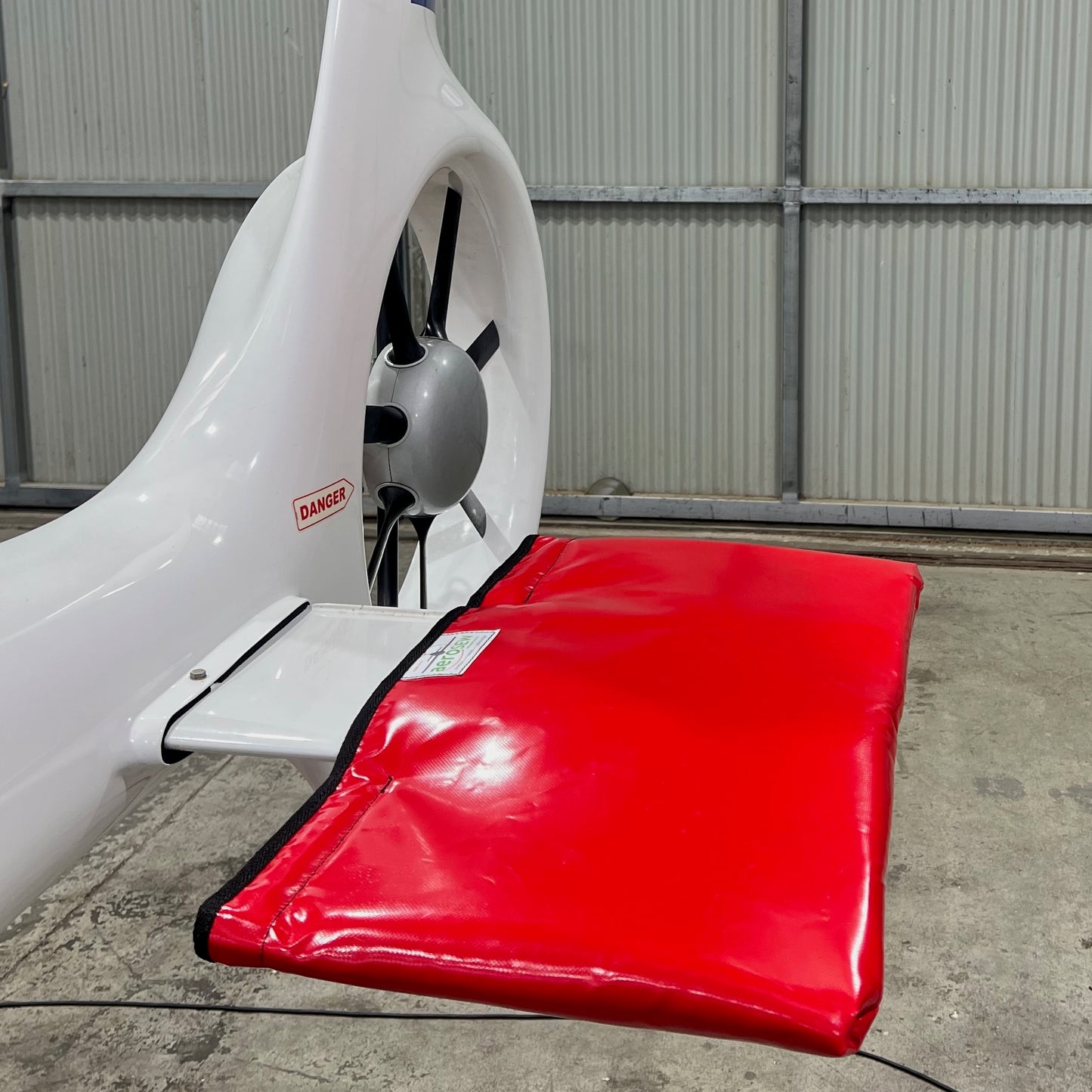 Red Aerosew padded cover fitted over the horizontal stabiliser of a white helicopter inside a hangar.