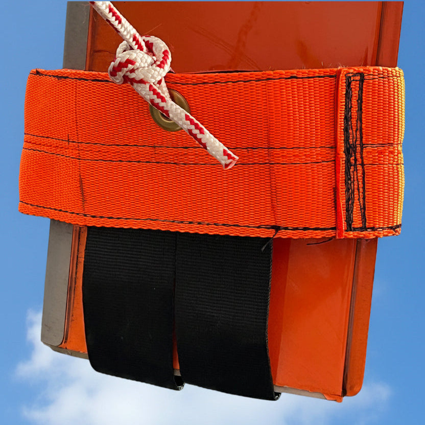 Orange Aerosew lightweight tie-down fitted around the tip of a Hughes 500 rotor blade against a blue sky.