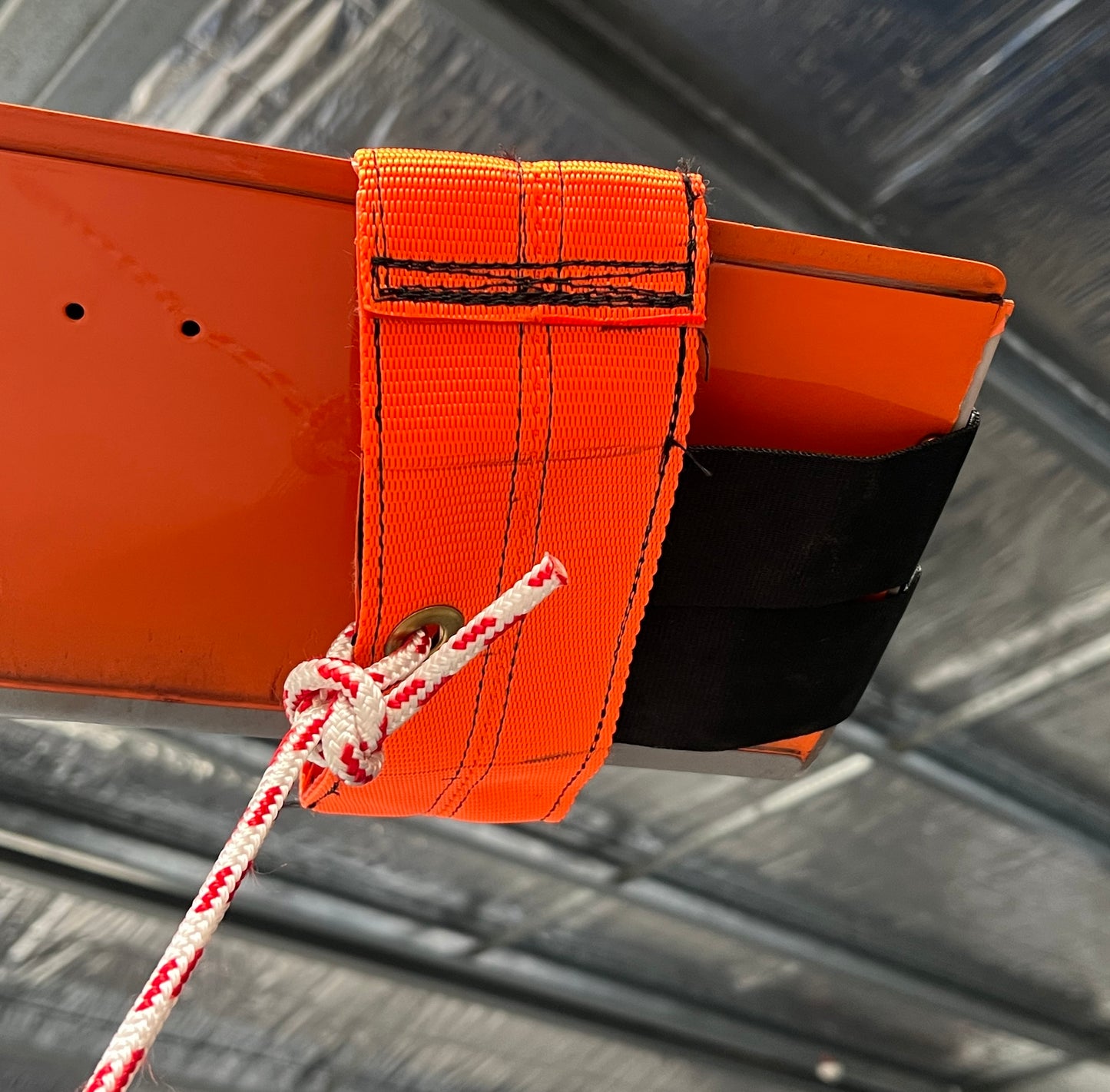 Close-up of an orange Hughes 500 lightweight rotor blade tie-down with black PVC reinforcement and red-and-white rope.