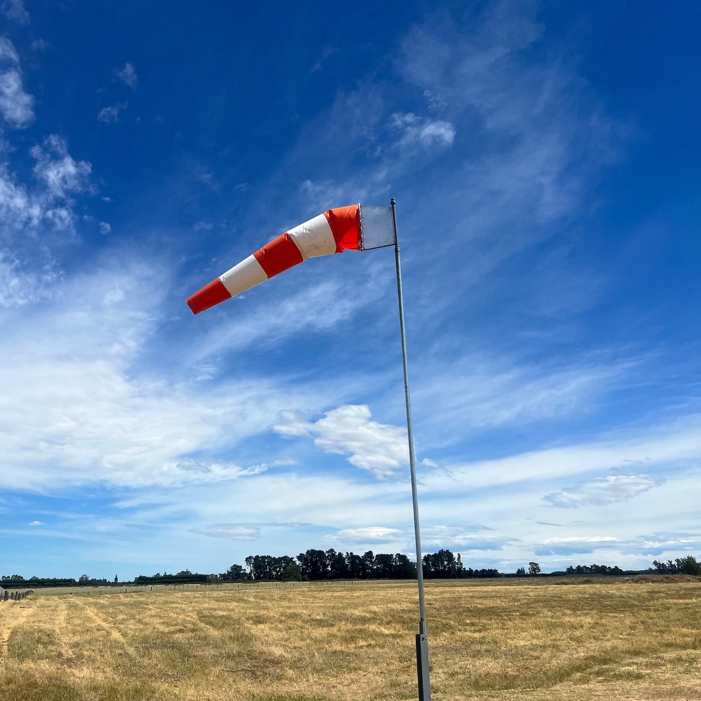 Red and white striped windsock against a blue sky with scattered clouds