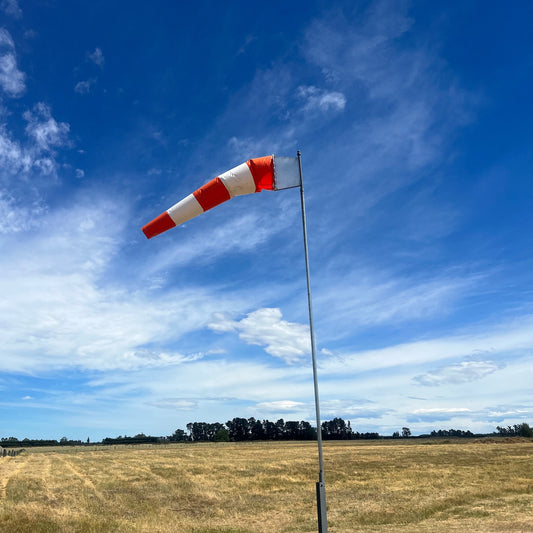 Red and white striped windsock against a blue sky with scattered clouds