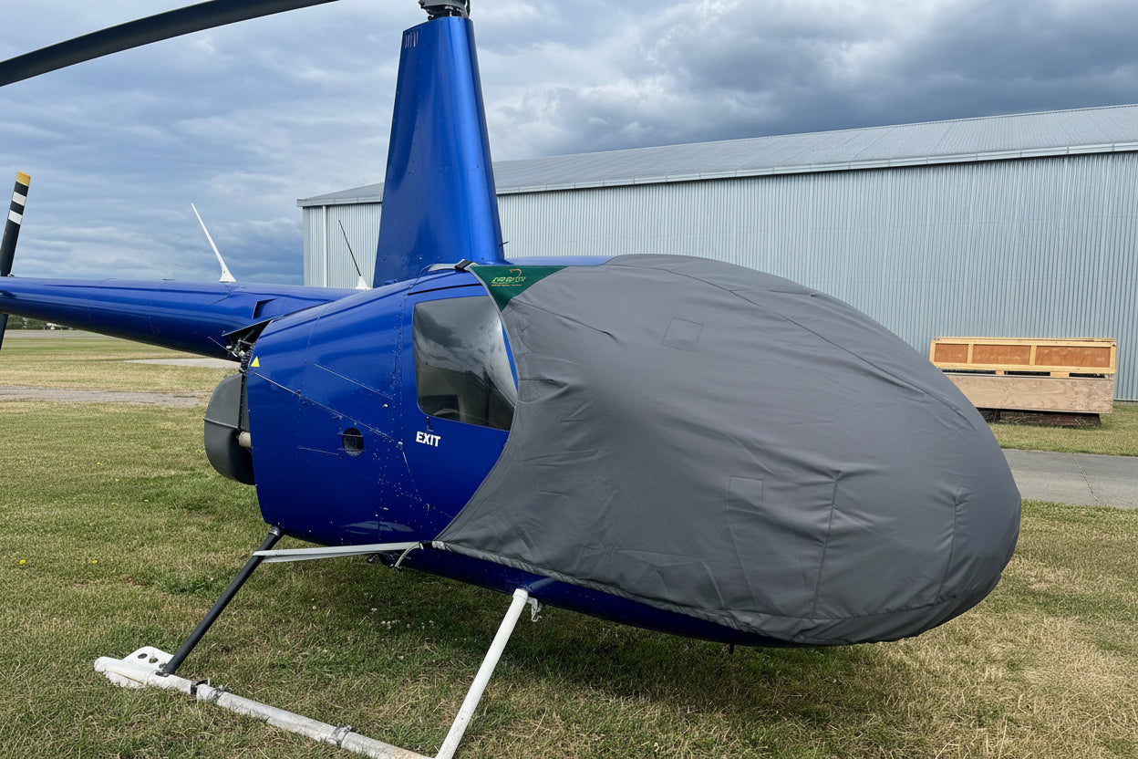 Blue R44 helicopter with a grey aerosew bubble cover on a grassy area with a building in the background